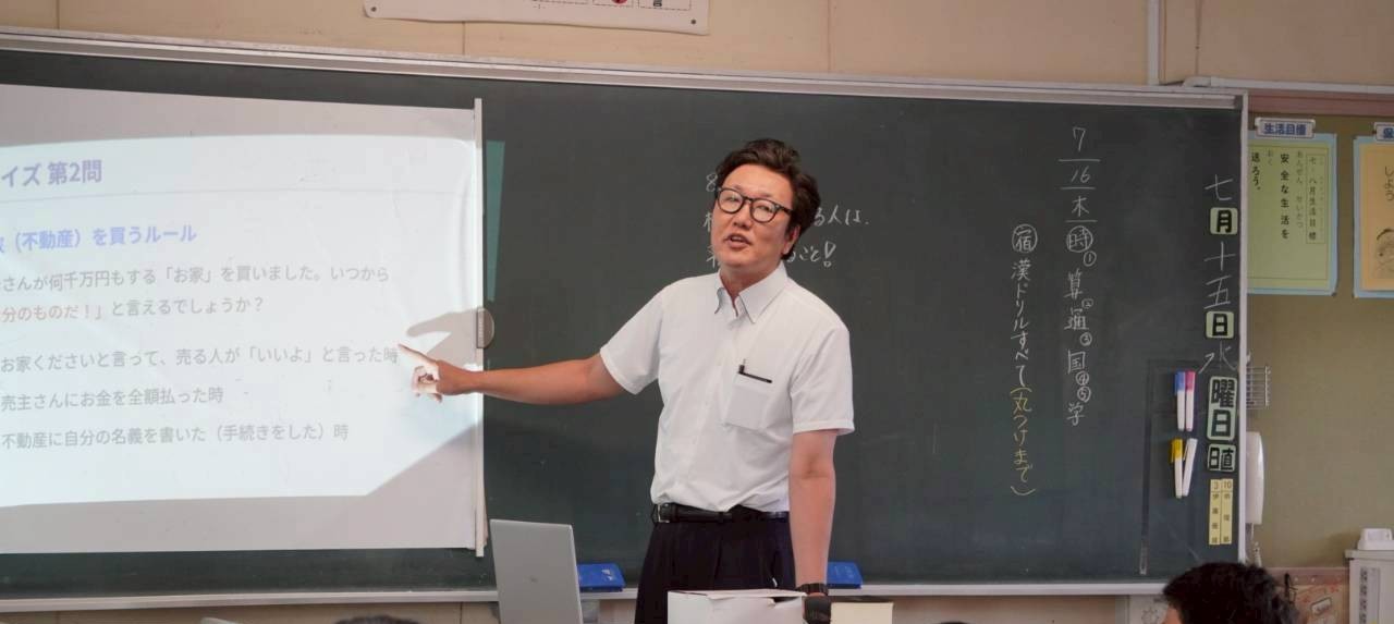 蟹江小学校での出張授業の様子。スクリーンの法律クイズを前に、5年生のみなさんに話す司法書士尾張